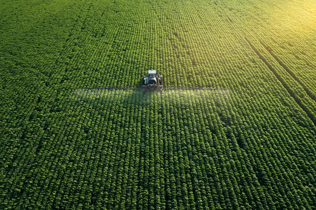 Aerial view of a tractor spraying crops in a lush green field, illustrating agricultural practices related to investment properties and business financing.