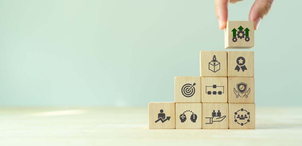 Hand placing wooden block with upward arrows and gears on a stacked arrangement of blocks, symbolizing growth and financial strategy in mortgage and refinancing context.